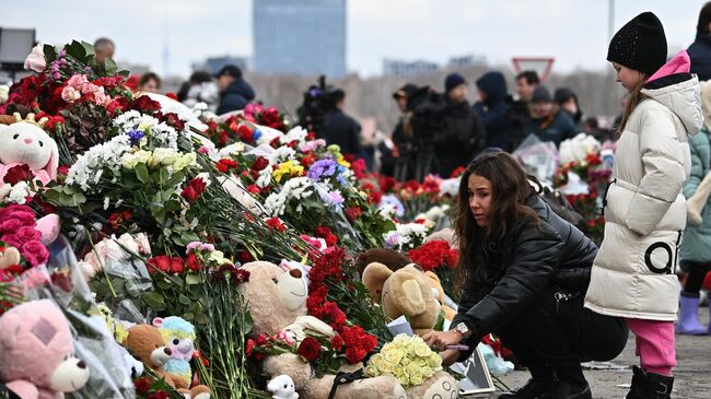 Девушка возлагает цветы у стихийного мемориала у здания концертного зала Крокус Сити Холл, где произошла стрельба и начался пожар